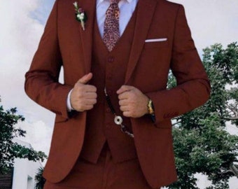 May include: A three-piece suit in a deep burgundy color. The suit features a single-breasted jacket with a notch lapel, a matching vest, and trousers. The jacket has a pocket square in the left breast pocket. The tie is a patterned silk tie with a brown and white design.
