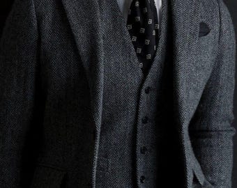 Può includere: Un abito grigio a spina di pesce con un gilet nero e una cravatta nera con un motivo geometrico bianco.
