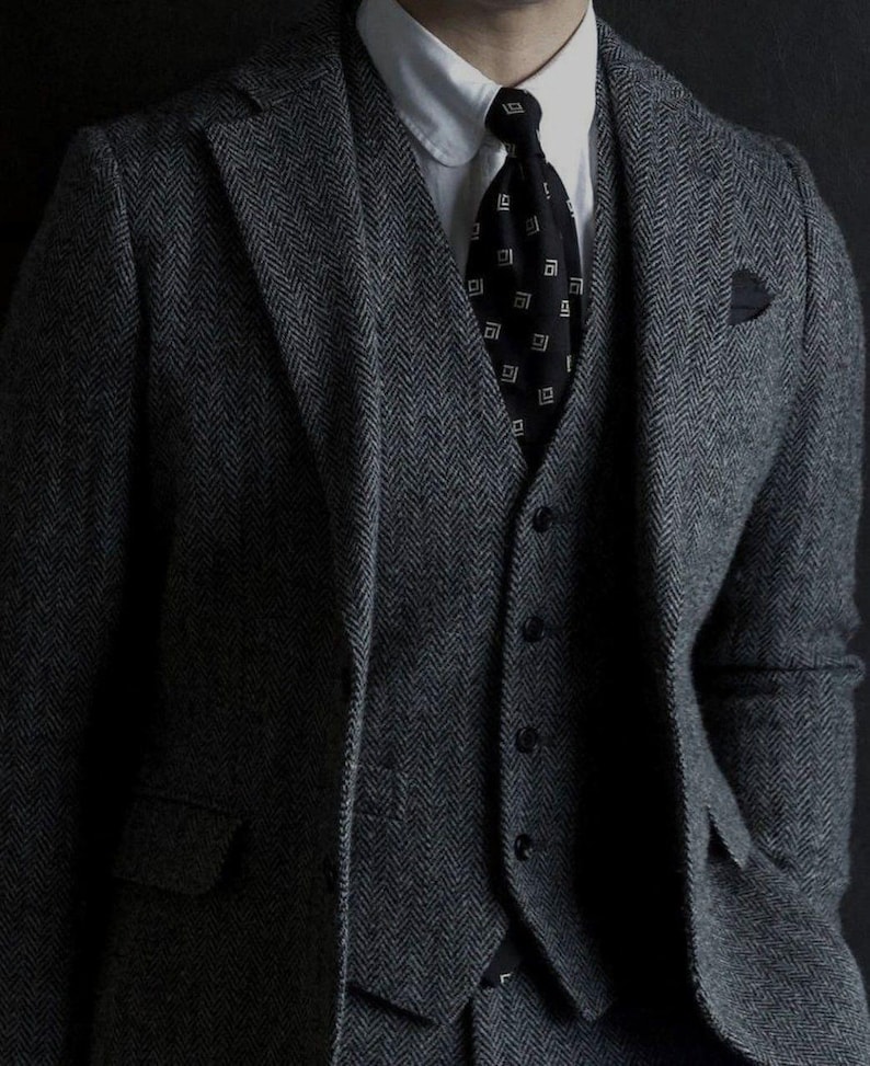 Peut inclure: Un costume gris &agrave; chevrons avec un gilet noir et une cravate noire &agrave; motif g&eacute;om&eacute;trique blanc.