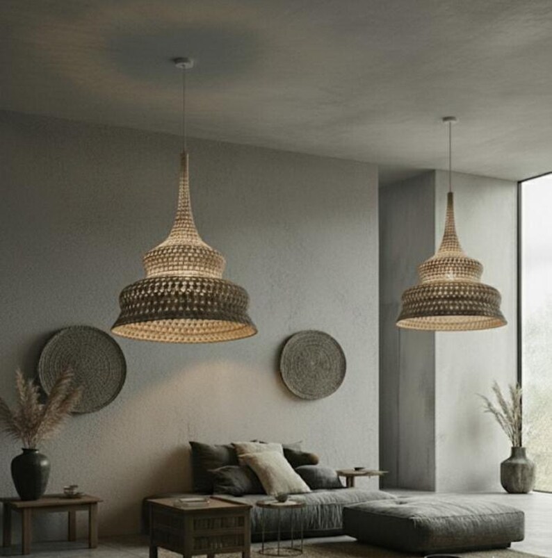 May include: Two woven pendant lights with a tiered design hang from the ceiling. The lampshades are a light brown color and have a textured appearance. The room is decorated in neutral tones with a sofa, decorative wall hangings, and vases.