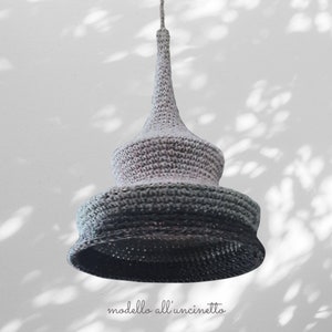 May include: A grey and black crocheted pendant light fixture with a pointed top and a wide, round base. The light fixture is hanging from a white ceiling.