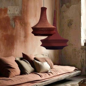 Può includere: Due grandi lampade a sospensione in crochet rosso pendono dal soffitto in una stanza rustica con un divano e cuscini. Il testo "cuci unconventional crochet Torino" è visibile sul muro.