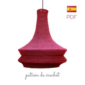 May include: A handmade, two-tone crochet lampshade in shades of pink and burgundy, suspended from a black cord. The lampshade has a flared, bell-like shape with a textured surface. The text "patrón de crochet" is written at the bottom.