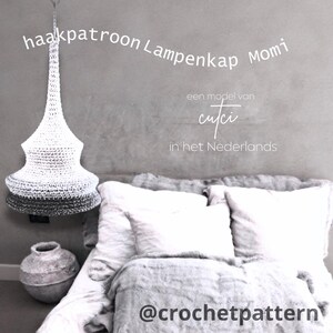 May include: A white and gray crocheted lampshade hangs from the ceiling. The lampshade has a conical shape with a gradient from white to gray. Text on the image reads "haakpatroon Lampenkap Momi" and "@crochetpattern".