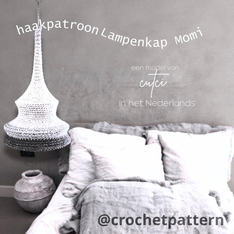 May include: A white and gray crocheted lampshade hangs from the ceiling. The lampshade has a conical shape with a gradient from white to gray. Text on the image reads "haakpatroon Lampenkap Momi" and "@crochetpattern".