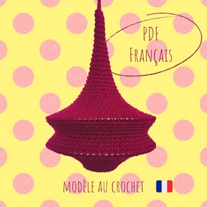 May include: A burgundy crochet lampshade with a conical top and a flared, star-shaped bottom. The text "PDF FRANÇAIS" is written in white, and the text "MODELE AU CROCHET" is written in white. The background is yellow with pink polka dots.