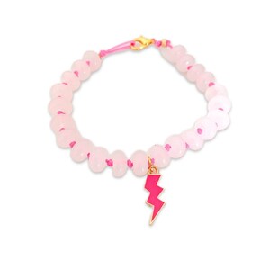 May include: A pink beaded bracelet with a pink lightning bolt charm. The bracelet is made with pink beads and a pink cord.