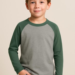 May include: A grey and forest green raglan-sleeved top. The long-sleeved shirt is worn by a young person, paired with blue jeans. The background is a solid, neutral colour.