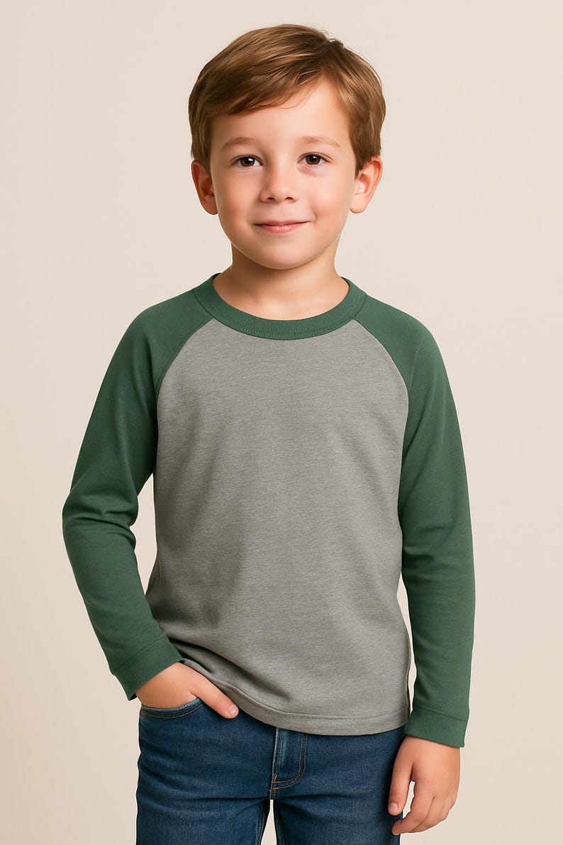 May include: A grey and forest green raglan-sleeved top. The long-sleeved shirt is worn by a young person, paired with blue jeans. The background is a solid, neutral colour.