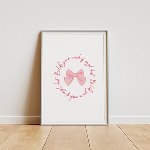 Puede incluir: Impresión artística enmarcada con una ilustración de lazo rosa en el centro, rodeada de texto rosa que dice "It's like you're made of angel dust". La obra de arte se presenta en un marco plateado.