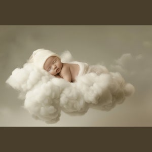 May include: A newborn baby wearing a white knitted hat sleeps peacefully on a fluffy white cloud.