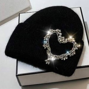 May include: Black knit beanie with a large rhinestone heart design.