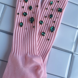 Peut inclure: Une paire de chaussettes roses avec des embellissements verts et dorés. Les chaussettes sont côtelées et ont un look décontracté.