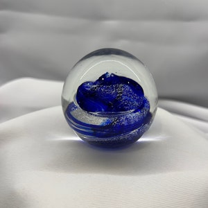 May include: A clear glass paperweight with a swirling blue and white design inside.