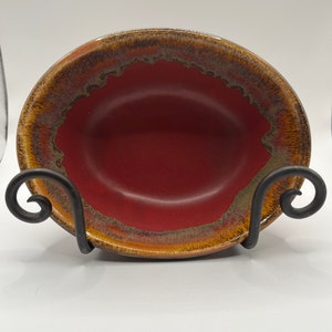 May include: A red ceramic bowl with a brown and gold rim. The bowl is sitting on a black metal stand.