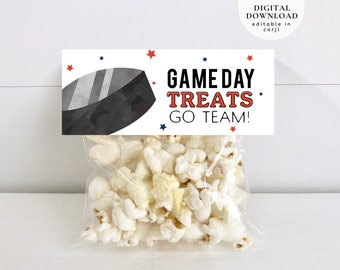 Puede incluir: Una etiqueta blanca imprimible con estrellas rojas y azules y el texto "GAME DAY TREATS GO TEAM!"  Una ilustración en blanco y negro de un disco de hockey está en el lado izquierdo de la etiqueta. La etiqueta está unida a una bolsa de plástico transparente llena de palomitas de maíz blancas.