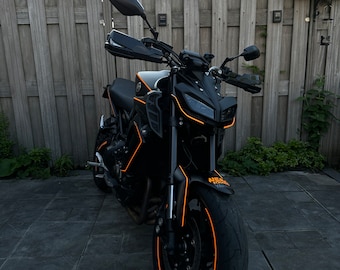 May include: A black motorcycle with orange accents. The motorcycle has a black seat, black handlebars, and a black front fender. The front tire has an orange stripe.