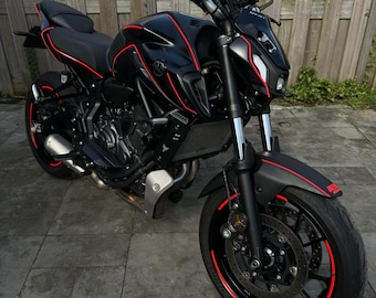 May include: A black motorcycle with red accents. The motorcycle has a black seat, black handlebars, and black wheels with red stripes. The motorcycle is parked on a gray concrete surface.