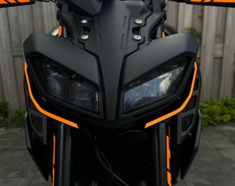 May include: A black motorcycle with orange accents. The motorcycle has a large front headlight and a black windshield.