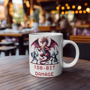 Op de afbeelding: Witte keramische mok met een gepixeld draakontwerp, ridders en de tekst "108-BIT DAMAGE" in het rood. De draak is rood met paarse vleugels en de ridders dragen zilveren harnassen. De mok heeft een gebogen handvat.