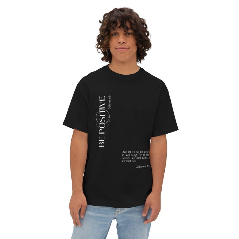 May include: Black t-shirt with the words "BE POSITIVE" in white vertical text, along with a Bible verse. The shirt is a classic crew neck style.