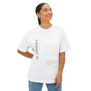 May include: White t-shirt with the words "BE POSITIVE" in a vertical design on the front. The shirt also features a quote from Galatians 6:9. The model is wearing blue jeans.