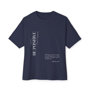 May include: Navy blue t-shirt with the words "BE POSITIVE" in white, along with the text "Galatians 6:9" and a quote. The shirt has a crew neck and short sleeves. A motivational tee for everyday wear.