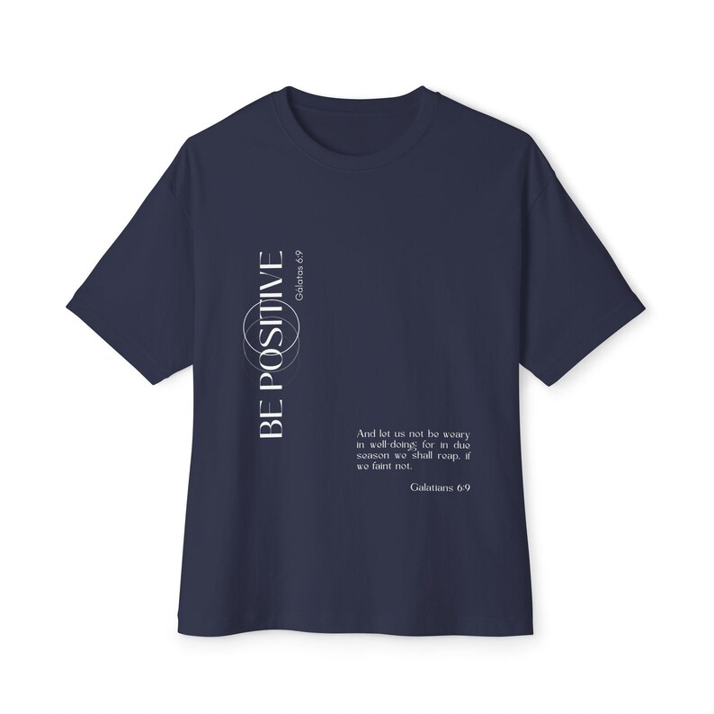 May include: Navy blue t-shirt with the words "BE POSITIVE" in white, along with the text "Galatians 6:9" and a quote. The shirt has a crew neck and short sleeves. A motivational tee for everyday wear.