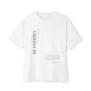 May include: White t-shirt with the words "BE POSITIVE" in black vertical text on the left side. The shirt also features a quote from Galatians 6:9 in a smaller font. A casual, short-sleeved tee.