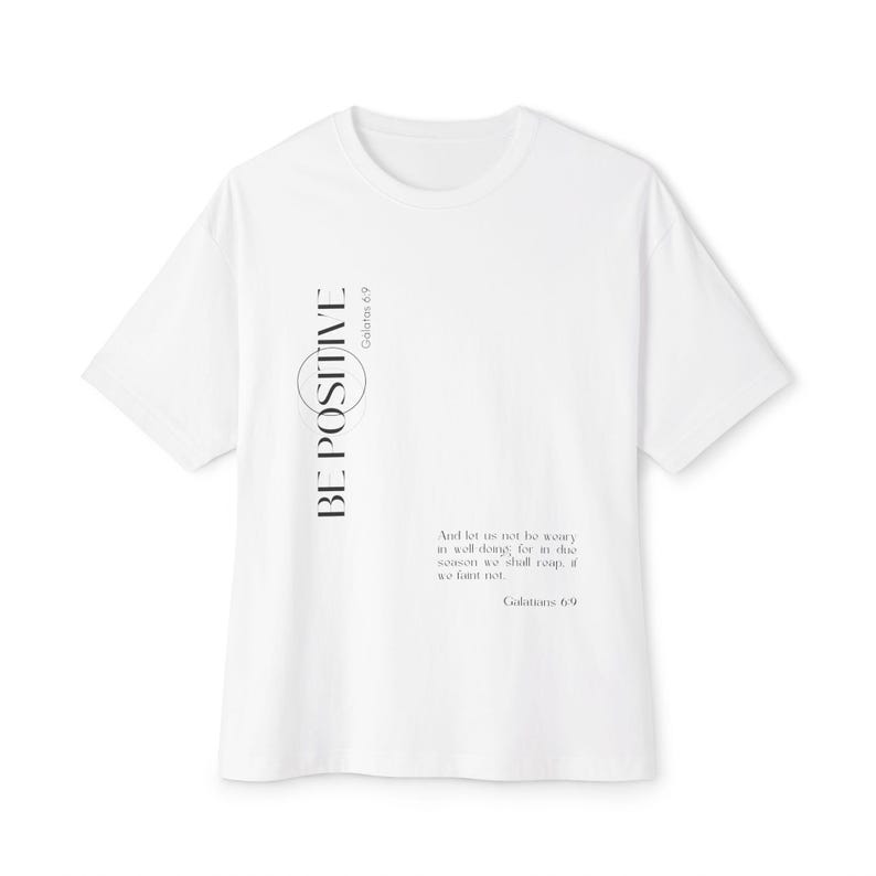 May include: White t-shirt with the words "BE POSITIVE" in black vertical text on the left side. The shirt also features a quote from Galatians 6:9 in a smaller font. A casual, short-sleeved tee.