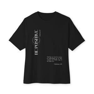 May include: Black t-shirt with the words "BE POSITIVE" in white, along with a quote from Galatians 6:9. The shirt has short sleeves and a crew neck. The text is vertically aligned on the left side of the shirt.