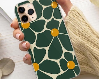 May include: A phone case with a green floral pattern featuring cream-coloured petals and yellow centres. The case is held by a person wearing a beige jumper. A pinecone and dried leaves are also visible.