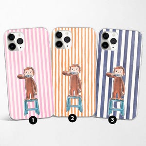 Op de afbeelding: Drie telefoonhoesjes met verticale streepjespatronen in roze, oranje en blauw. Elke hoes heeft een cartoon aap die zijn tanden poetst terwijl hij op een kleine blauwe kruk staat. De hoesjes zijn ontworpen voor een smartphone.