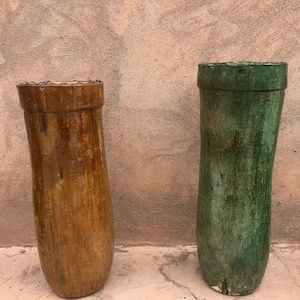 May include: Two tall, cylindrical vases. One is a warm, earthy brown with a textured surface. The other is a vibrant green with a weathered appearance. Both have a slightly flared rim and a rustic aesthetic, suitable for home decor.