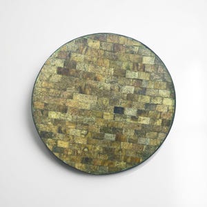 Puede incluir: Una bandeja decorativa redonda con un diseño de mosaico. La superficie está compuesta por pequeñas piezas rectangulares en tonos dorados, marrones y verdes, que simulan un patrón de ladrillos. La bandeja tiene un borde verde oscuro.