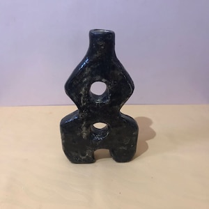 May include: Black ceramic vase with two circular openings. The vase is in a minimalist style and has a unique, abstract shape.