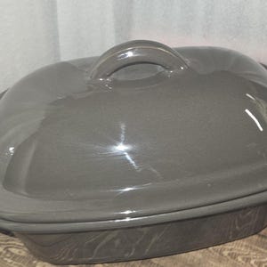 May include: A gray ceramic casserole dish with a lid. The dish has a rounded shape with a handle on the lid. The dish is approximately 12 inches long and 8 inches wide.