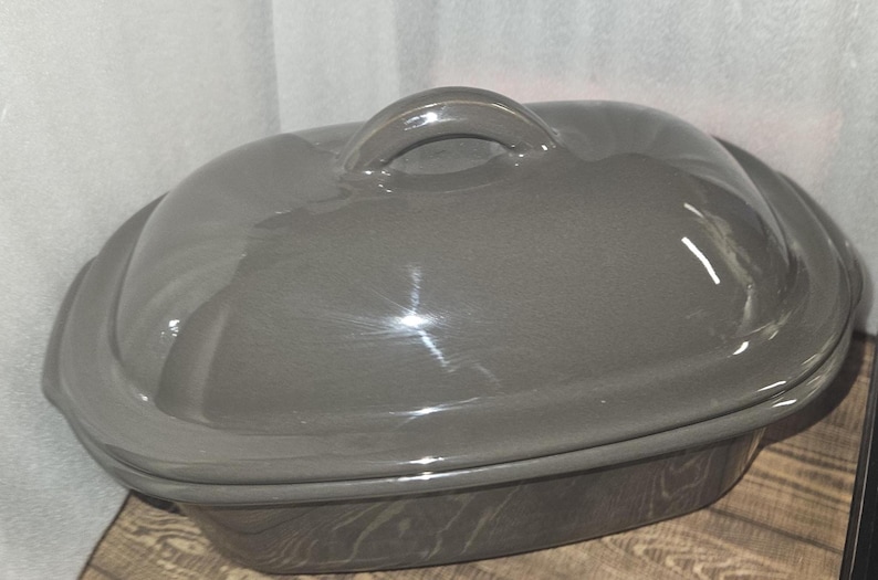 May include: A gray ceramic casserole dish with a lid. The dish has a rounded shape with a handle on the lid. The dish is approximately 12 inches long and 8 inches wide.
