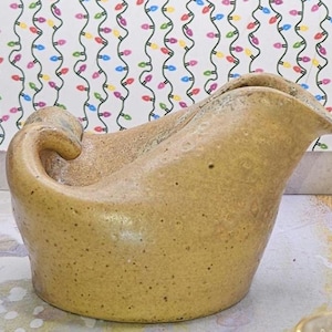 Może przedstawiać: Ceramiczny dzbanek o unikalnym, organicznym kształcie. Dzbanek jest jasnobrązowy z pstrokatą glazurą.