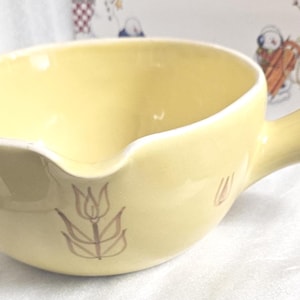 Könnte beinhalten: Eine hellgelbe Keramik-Suppenschüssel mit Griff und Ausguss. Die Schüssel hat ein braunes Tulpenmuster und einen weißen Rand. Der Griff ist gebogen und die Schüssel ist wahrscheinlich Vintage.