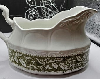 Puede incluir: Salsera de cerámica blanca con un diseño floral verde y blanco. La salsera tiene una base ancha y redondeada y un pico en un lado.