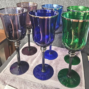Puede incluir: Seis copas de vino con bordes dorados. Las copas son de varios colores, incluyendo morado, azul y verde.