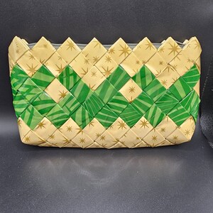 May include: A woven pouch with a zip closure. The pouch features a repeating pattern of green and gold paper strips. The gold strips are decorated with small star shapes. The zip is grey.
