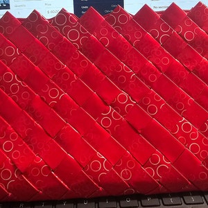 K&ouml;nnte beinhalten: Eine rote Clutch mit gewebtem Design. Die Clutch besteht aus rotem Material mit einem sich wiederholenden Muster aus wei&szlig;en Kreisen. Das gewebte Muster erzeugt eine strukturierte Oberfl&auml;che. Die Clutch ist rechteckig und hat einen Rei&szlig;verschluss.