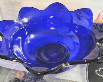 May include: A deep cobalt blue glass bowl featuring a scalloped, flower-like rim with multiple rounded petals. The bowl has a smooth, reflective surface and a circular base, showcasing a vibrant, translucent color throughout the entire piece.
