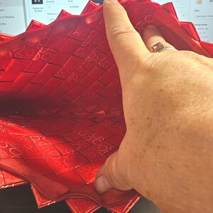 K&ouml;nnte beinhalten: Eine rote, gewebte Rei&szlig;verschlusstasche mit einem geometrischen Muster. Das Innere der Tasche ist sichtbar und zeigt ein &auml;hnliches Muster. Der Rei&szlig;verschluss ist dunkelrot. Die Tasche ist ge&ouml;ffnet und gibt den Blick ins Innere frei.