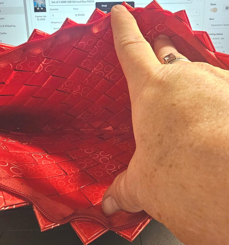 K&ouml;nnte beinhalten: Eine rote, gewebte Rei&szlig;verschlusstasche mit einem geometrischen Muster. Das Innere der Tasche ist sichtbar und zeigt ein &auml;hnliches Muster. Der Rei&szlig;verschluss ist dunkelrot. Die Tasche ist ge&ouml;ffnet und gibt den Blick ins Innere frei.