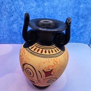 May include: A yellow and black ceramic vase with a geometric design. The vase has two black handles and a black rim.