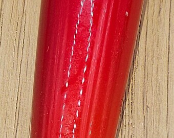 May include: A red glass pepper with a green glass stem. The pepper has a glossy finish and a white line down the center.