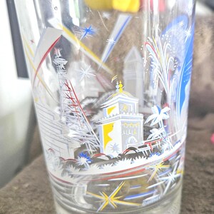 May include: Clear glass with a colorful illustration of a cityscape, fireworks, and the text "World Remember". The design includes white, yellow, red, and blue accents. The glass has a slightly flared shape.
